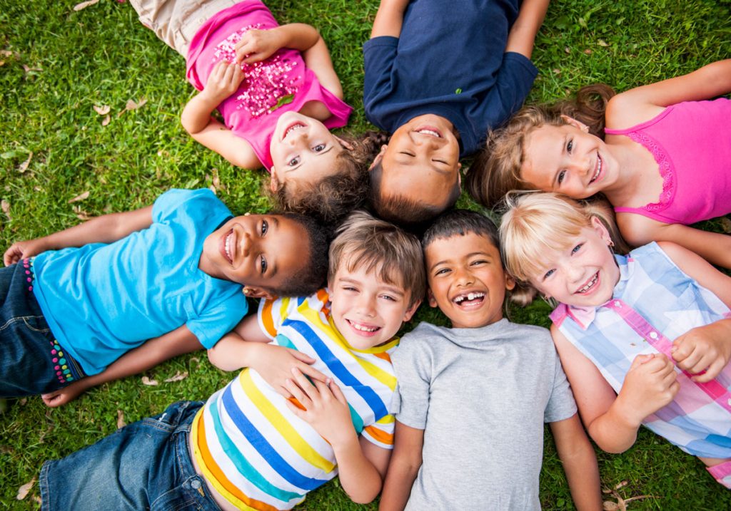 group of multi-racial students lying in the grass in a circle smiling