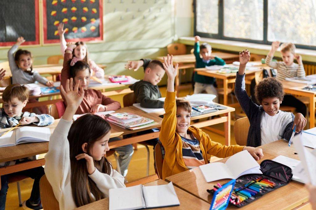 bunch of elementary students sitting at their desk raising their hands