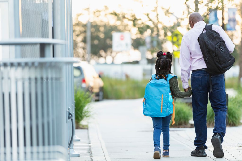 father holding hand of daughter while walking her to school